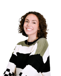 "A professional headshot of a woman with curly brown hair, wearing a striped sweater with black, white, and olive green blocks. She is smiling and facing the camera against a plain white background.