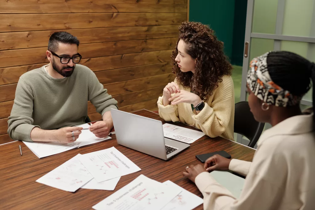 Diverse group of coworkers having a meeting, discussing documents and strategies related to Texas estate protection, seated at a wooden table with a laptop.