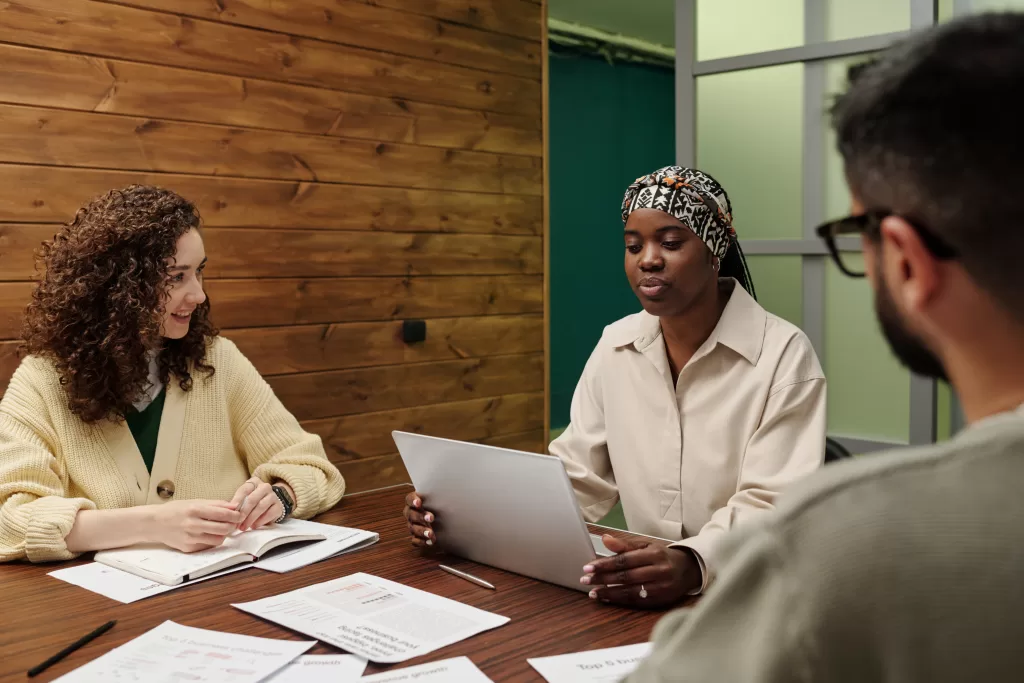 Two women and a man in a meeting discussing estate planning strategies, with documents and a laptop on a wooden table.