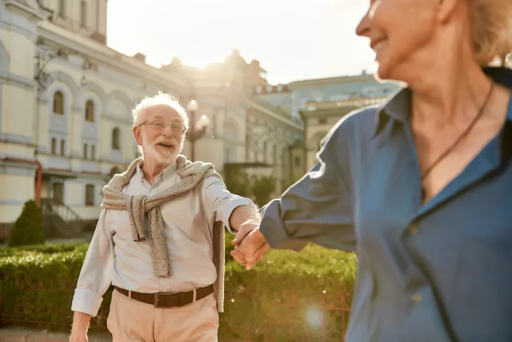 Come with me. Beautiful and happy elderly couple holding hands and smiling while spending time