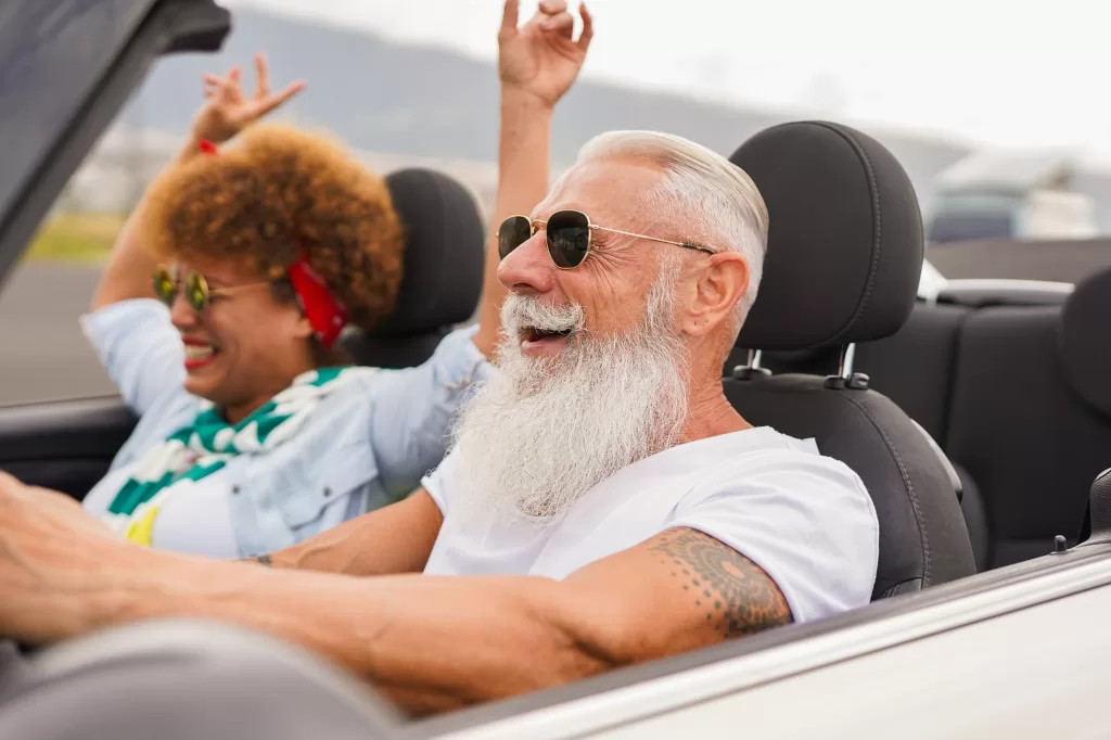 Happy elderly people having fun during road trip vacation inside cabriolet car